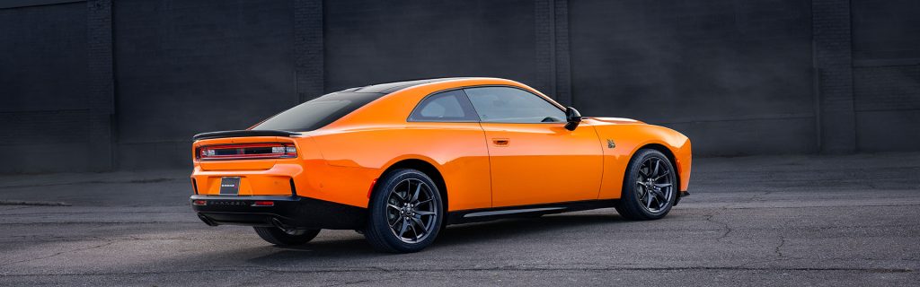 An orange Dodge Charger parked against a dark wall.